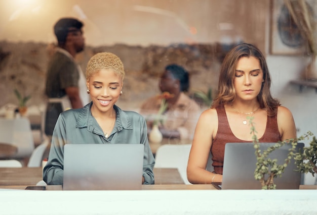 Trabalhando laptop e mulheres de negócios na janela do café para trabalho remoto, carreira freelance e rede Tecnologia de comunicação e trabalhadoras com computador para relatório de projeto e digitação de e-mail