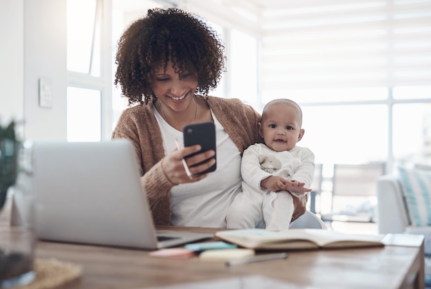 Trabalhando para um futuro financeiramente seguro Foto de uma jovem usando um smartphone e laptop enquanto cuidava de sua adorável bebê em casa