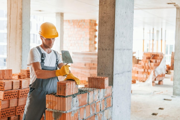 Foto trabalhando usando tijolos jovem de uniforme na construção durante o dia