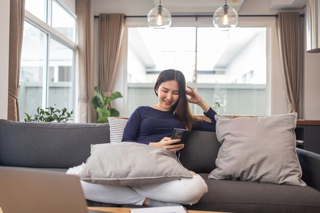 Trabalhe a partir do conceito de casa, uma jovem empresária sentada em um sofá aconchegante usando seu telefone celular, conversando com os clientes.