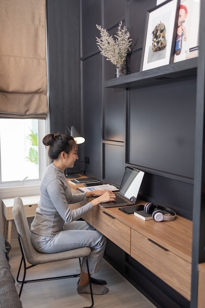 Trabalhe a partir do conceito de casa, uma jovem garota com um coque fazendo seu trabalho remoto no quarto dela.