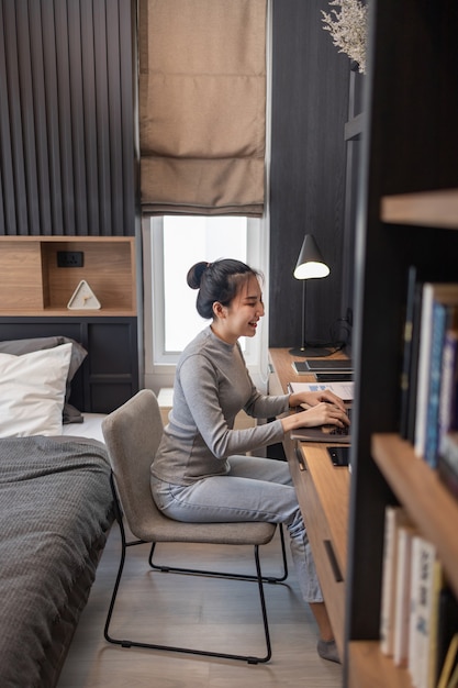 Trabalhe a partir do conceito de casa, uma jovem garota com um coque fazendo seu trabalho remoto no quarto dela.