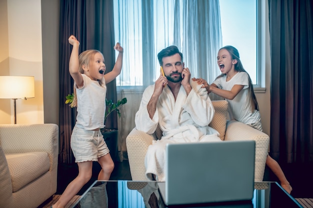 Trabalhe em casa. Duas garotas se divertindo e atrapalhando seu pai que trabalha