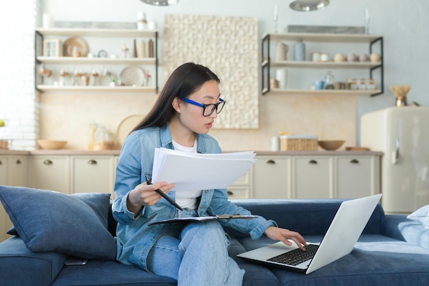 Trabalhe em casa online jovem contadora asiática trabalhando em casa sentada no sofá com um laptop