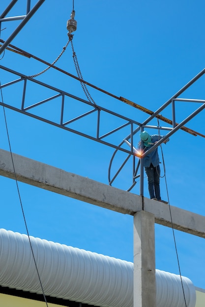 Trabalhe na altura, estrutura da soldadura do homem do telhado da fábrica no canteiro de obras.