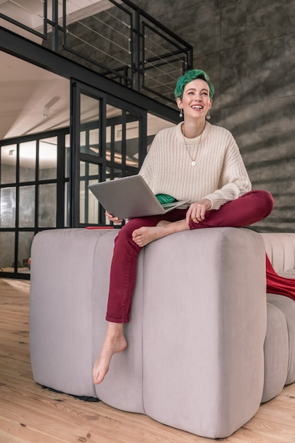 Trabalhe no laptop. Trabalhador remoto atraente de cabelo verde se sentindo feliz enquanto trabalha em casa em seu laptop