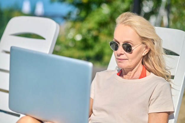 Trabalhe remotamente. Mulher loira bonita com um laptop sentada em uma espreguiçadeira