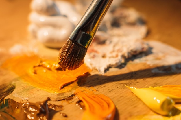 Foto trabalho de artista pintura de arte artesanato profissional pincel misturando óleo branco laranja ou cores de tinta acrílica na paleta de madeira manchada antiga