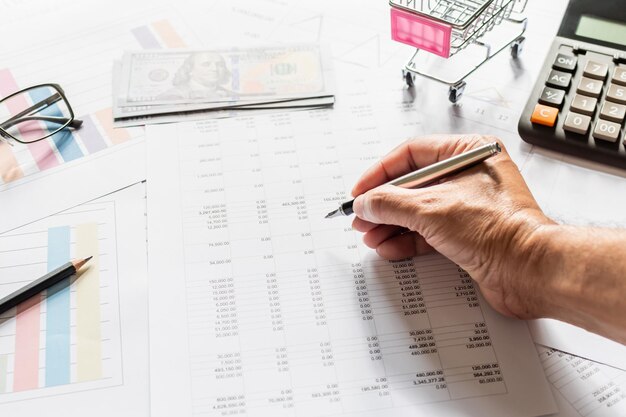 Trabalho de contabilidade financeira em casa Closeup Mans mão segurando uma caneta examinando números de contabilidade Números em papel e calculadora Muitos números gráfico lápis óculos em papel fundo desfocado xA