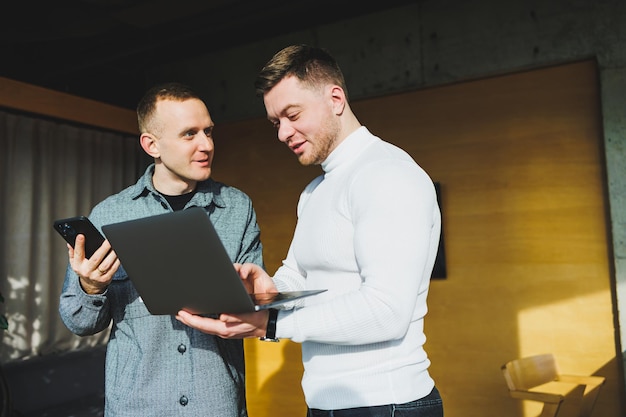 Trabalho de dois colegas do sexo masculino no escritório juntos enquanto trocam ideias com o laptop na sala de reuniões e analisam esquemas de trabalho Trabalho em um escritório moderno e espaçoso