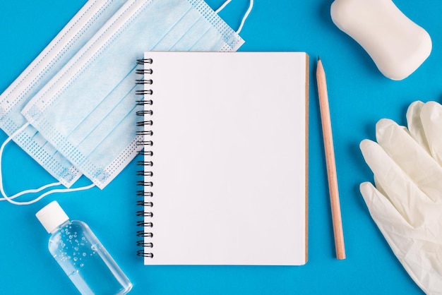 Trabalho de estudo de educação do conceito de casa. layout de topo flatlay close-up foto de página de papel transparente em branco vazio bloco de desenho desinfecção garrafa de borracha luvas de rosto máscara médica cirúrgica na mesa