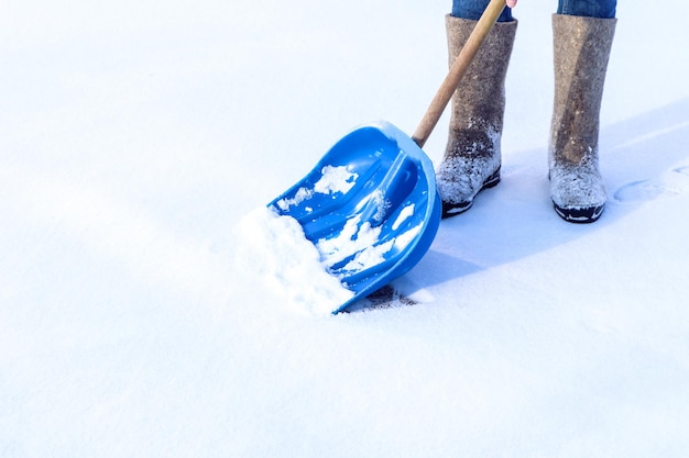 Trabalho de inverno no local que limpamos a neve Pá azul para remoção de neve no fundo das botas de feltro espaço de vista lateral para texto