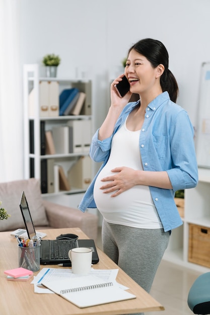 trabalho de negócios de gravidez e conceito de tecnologia. sorridente empresária grávida alegre com smartphone em pé na mesa do escritório. senhora de maternidade alegre falando no celular no escritório em casa