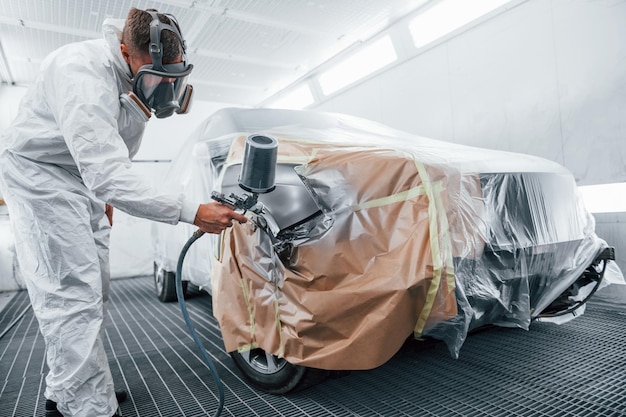 Trabalho de pintura em andamento reparador de automóveis caucasiano em uniforme trabalha na garagem