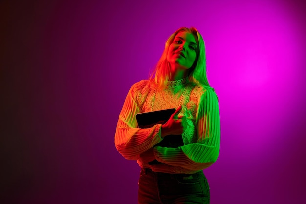 Trabalho e educação freelancer online Jovem mulher posando com tablet sobre fundo de estúdio magenta em luz neon verde Conceito de estilo de vida de emoções