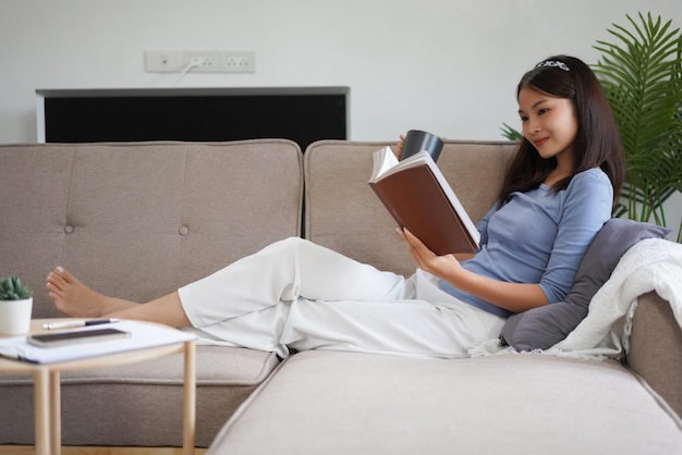 Trabalho em casa As mulheres de negócios lêem um livro e bebem café enquanto estão deitadas no sofá para relaxar