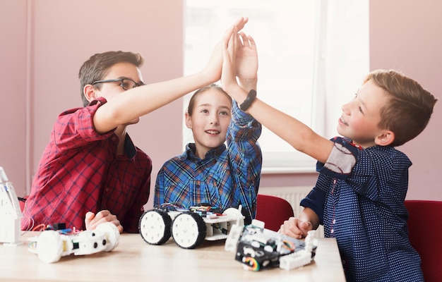 Trabalho em equipe bem-sucedido. crianças felizes construindo robôs e dando mais cinco na aula de ciências. desenvolvimento inicial, faça você mesmo, inovação, educação integrada, conceito de tecnologia moderna