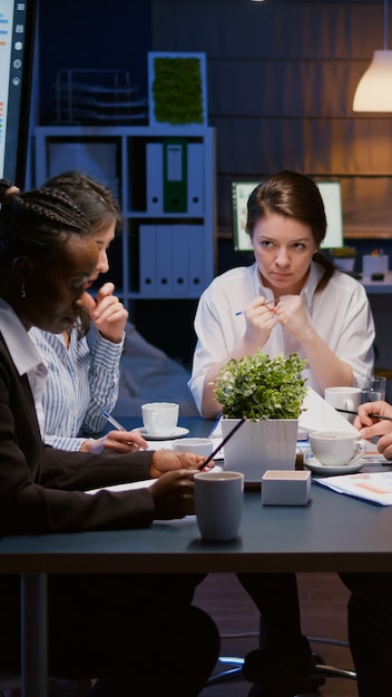 Trabalho em equipe de negócios multiétnicos diversos sobrecarregando na sala de reuniões do escritório, analisando gráficos financeiros ...