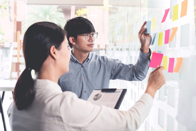 Trabalho em equipe de negócios na reunião e nota adesiva na placa do espelho discutindo com a equipe na sala de escritório para coletar algum plano de brainstorming de ideia.