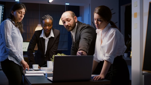 Trabalho em equipe diversificado, verificando apresentação de gerenciamento no laptop