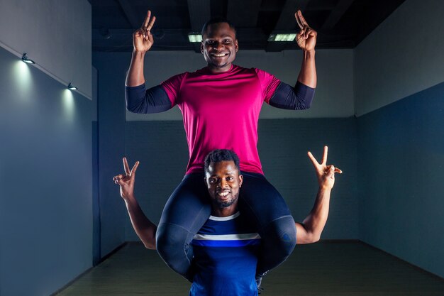 Trabalho em equipe dois bonito desportista afro-americano no boxe em um fundo preto no ginásio, treinador e ala praticando boxe