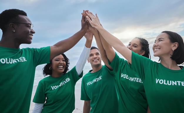 Trabalho em equipe, high five e voluntariado com pessoas na praia para sustentabilidade ambiental e mudança climática Dia da Terra de caridade e comunidade com amigos para apoiar a diversidade e a conscientização sobre a poluição