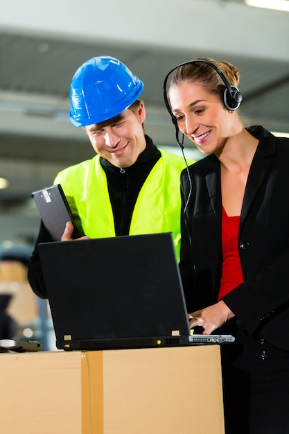 Trabalho em equipe, motorista de armazém ou empilhadeira e supervisor feminino com laptop, fone de ouvido e telefone celular, no armazém da empresa de encaminhamento de carga uma empilhadeira