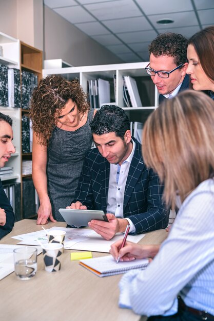 Trabalho em equipe procurando documento em tablet eletrônico ao redor do chefe de negócios na sede da empresa