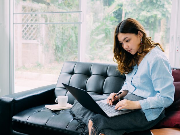 Trabalho em linha do Internet da mulher consideravelmente asiática em casa e relaxe o estilo de vida com seu labtop