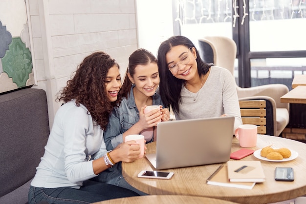 Trabalho feito. Três alunos alegres e entusiasmados olhando para a tela enquanto riem e usam o laptop