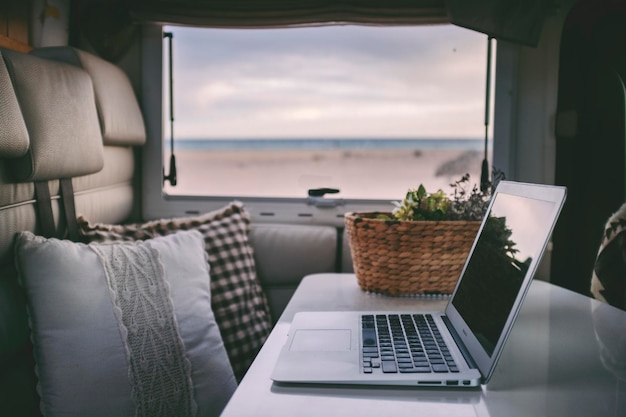 Trabalho onilne remoto e conceito de viagem de trabalho inteligente com computador portátil dentro de um interior de van campista com vista para a praia. Liberdade do estilo de vida moderno do escritório para vida e pessoas alternativas