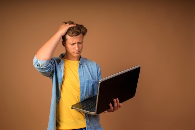 Foto trabalho remoto moderno. retrato de um jovem com um laptop nas mãos em uma parede bege