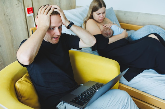 Trabalho remoto on-line Um pai feliz está trabalhando em um laptop enquanto sua esposa está cuidando da criança Trabalhando em casa para ser pai e trabalhar remotamente Amamentando um bebê recém-nascido