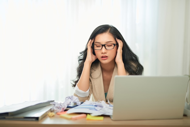 Trabalho remoto, tecnologia e conceito de pessoas - jovem estressada com laptop e papéis trabalhando em casa