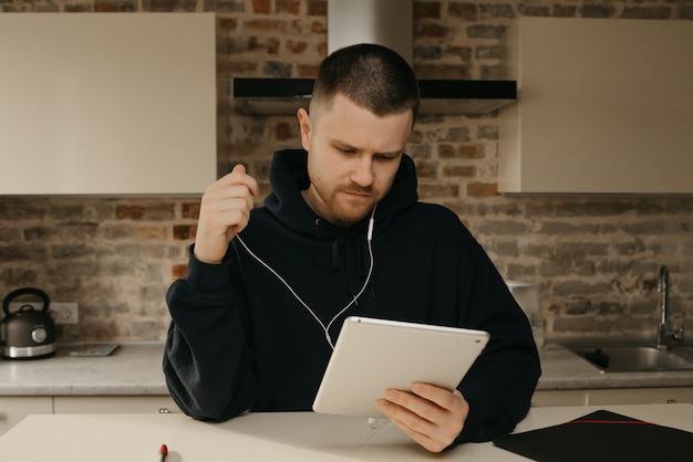 Trabalho remoto. Um homem com barba trabalhando remotamente em seu tablet. Um homem de negócios conversando com seus colegas sobre um negócio por uma videoconferência.