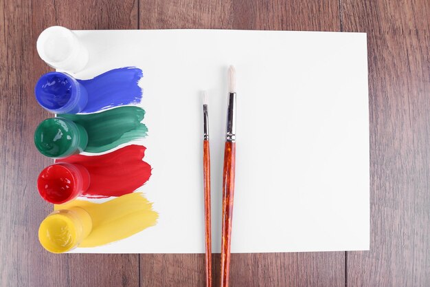 Foto traços de tinta colorida com pincel e latas de tinta na folha de papel branca sobre fundo de mesa de madeira