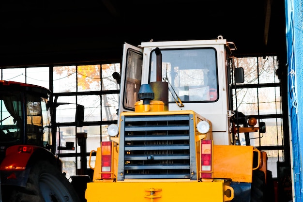 Tractor amarillo grande y potente con ruedas grandes en el garaje del almacén del hangar con puertas abiertas