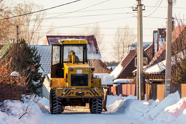 El tractor amarillo limpia la carretera de la nieve en un pequeño pueblo rural.