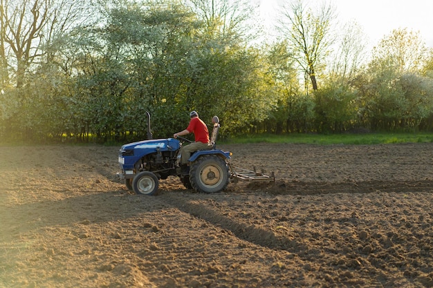 El tractor atraviesa el campo y cultiva la tierra El vehículo agrícola trabaja en el campo La siembra es el proceso de plantar semillas en el suelo como parte de la primavera temprana