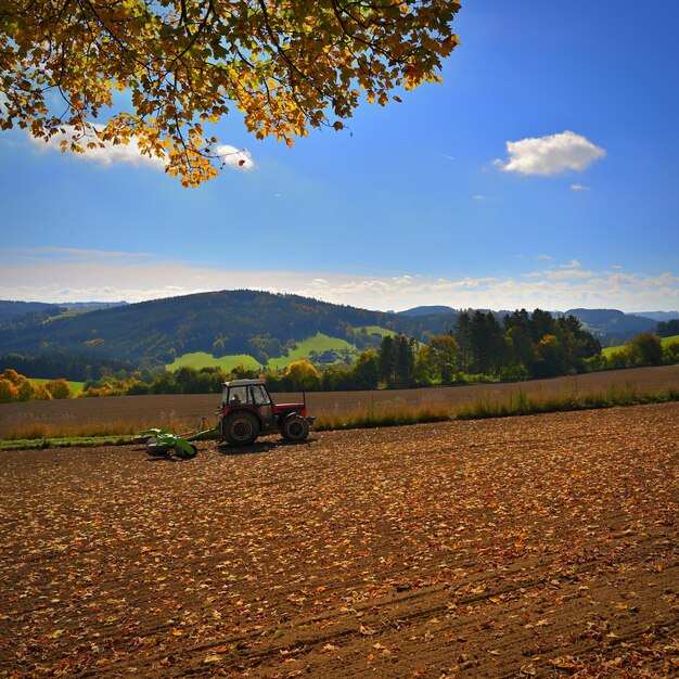 Tractor en el campo Hermosa naturaleza otoñal con paisaje en la República Checa Árboles coloridos con cielo azul y sol Antecedentes para el otoño y la agricultura