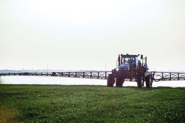 Foto tractor com a ajuda de um pulverizador pulveriza fertilizantes líquidos em trigo jovem no campo