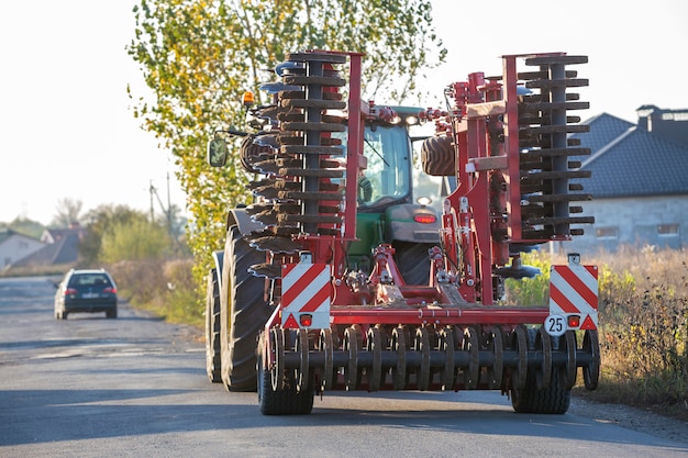 El tractor se combina con las gradas de discos que conducen a lo largo del camino rural en un día soleado.