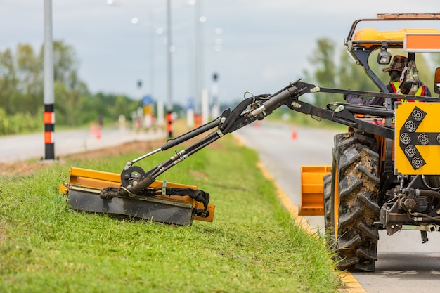 Foto tractor con un cortacésped mecánico cortando césped al lado de la carretera de asfalto