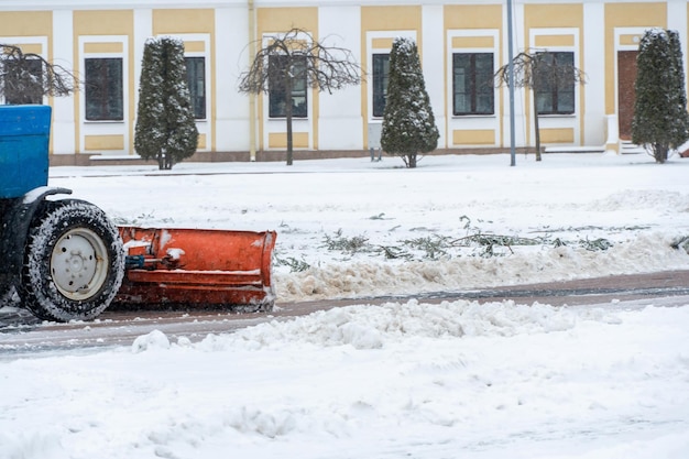 Un tractor limpia la nieve en la ciudad en invierno después de una nevada Limpiando las calles de la ciudad de la nieve Conductor del tractor en el trabajo en la plaza de la ciudad durante una tormenta de nieve