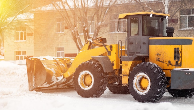 El tractor naranja limpia la nieve de la carretera y la carga en el camión. limpieza de caminos