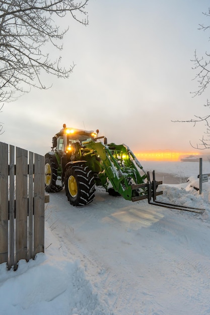Un tractor en la nieve con la puesta de sol detrás de él