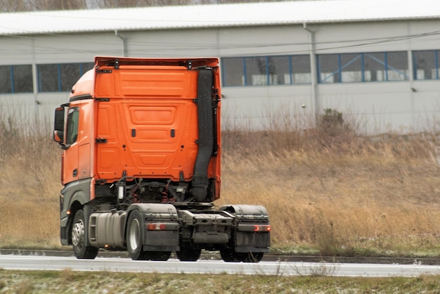 Un tractor sin remolque en la autopista Un camión brilla bajo la suave luz del sol mientras viaja a lo largo de una carretera tranquila bordeada por hierba silvestre y un edificio lejano Cabina de camión potente moderno