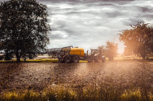 Foto un tractor rocía un campo con un árbol al fondo