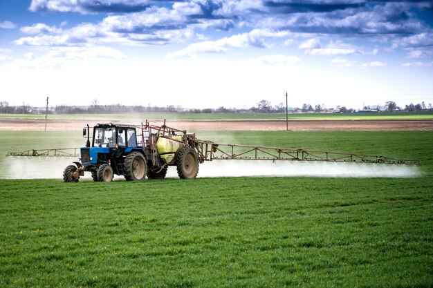 Un tractor rocía un campo con suplementos de crecimiento y destruirá las enfermedades de las plantas. Agricultura. Proporcionar comida.