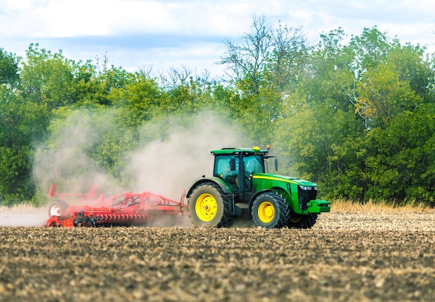 Un tractor verde está trabajando en el campo. Cultivo del suelo. Trabajo agrícola.